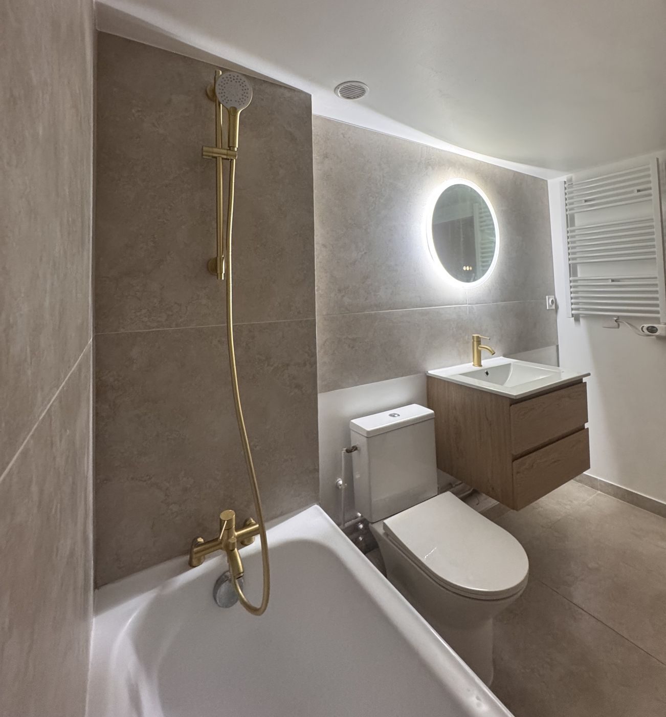 Salle de bain rénovée : baignoire, robinetterie dorée, meuble vasque bois et miroir lumineux